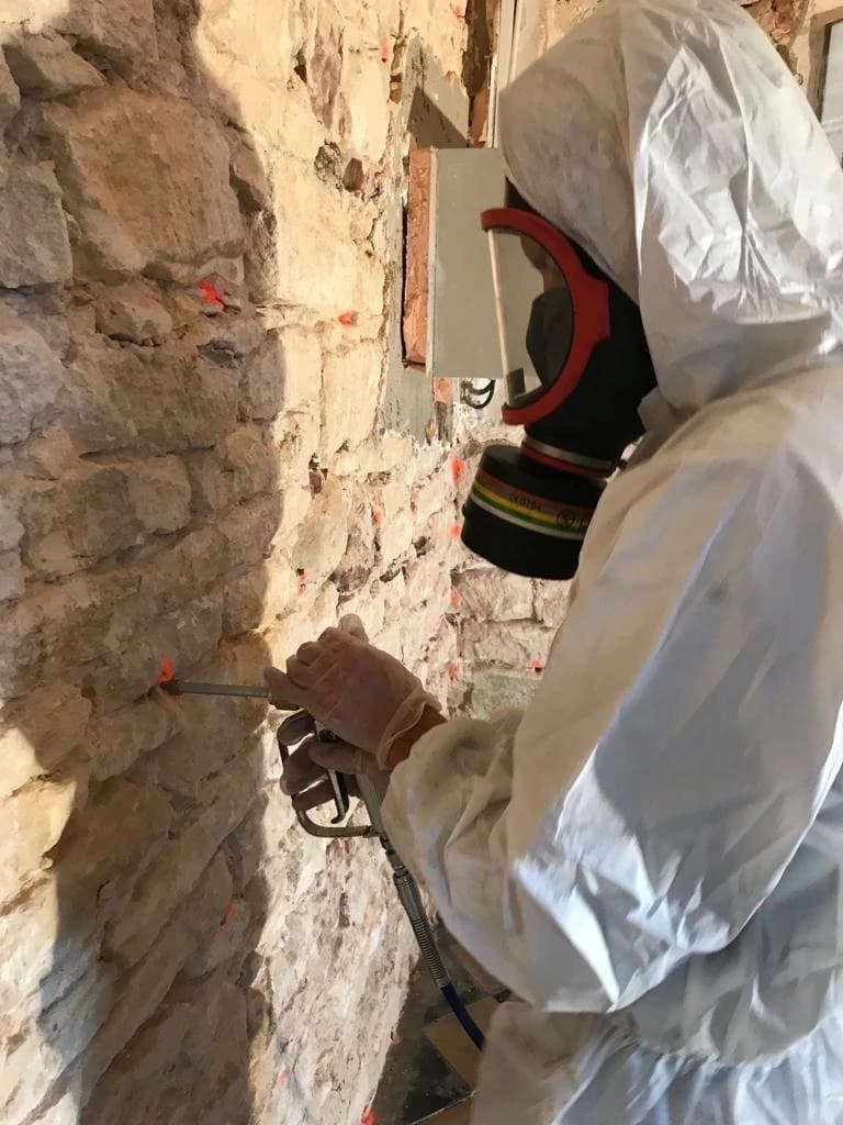 Technicien en combinaison intervenant sur une maçonnerie atteinte de mérule