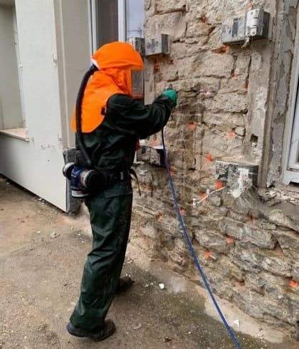 Technicien en tenue de protection traitant un mur contre la mérule